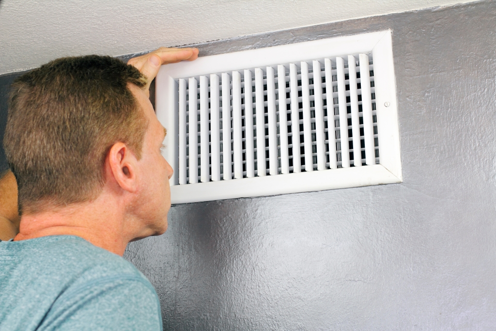 Man checking an outflow air vent grid and duct.